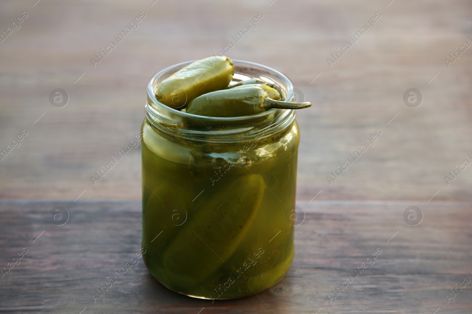 Photo of Glass jar of pickled green jalapeno peppers on wooden table, closeup