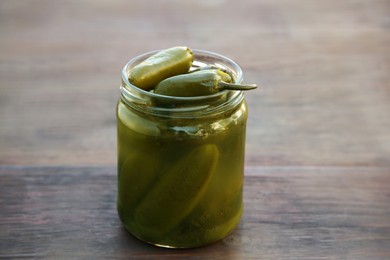 Photo of Glass jar of pickled green jalapeno peppers on wooden table, closeup