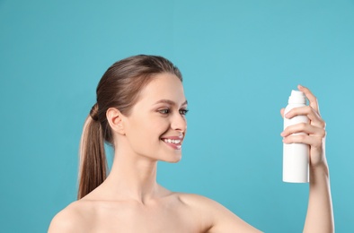 Young woman with bottle of thermal water on color background. Cosmetic product