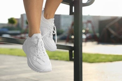 Photo of Woman in stylish sneakers sitting on railing outdoors, closeup. Space for text