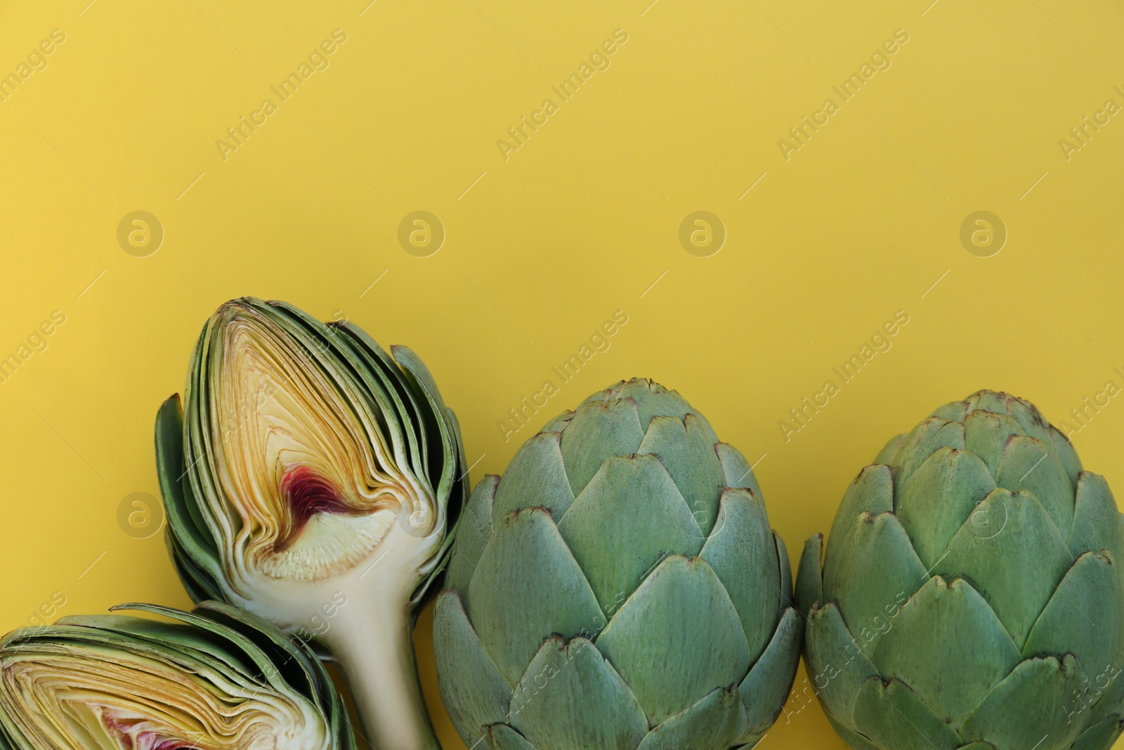 Photo of Cut and whole fresh raw artichokes on yellow background, flat lay. Space for text