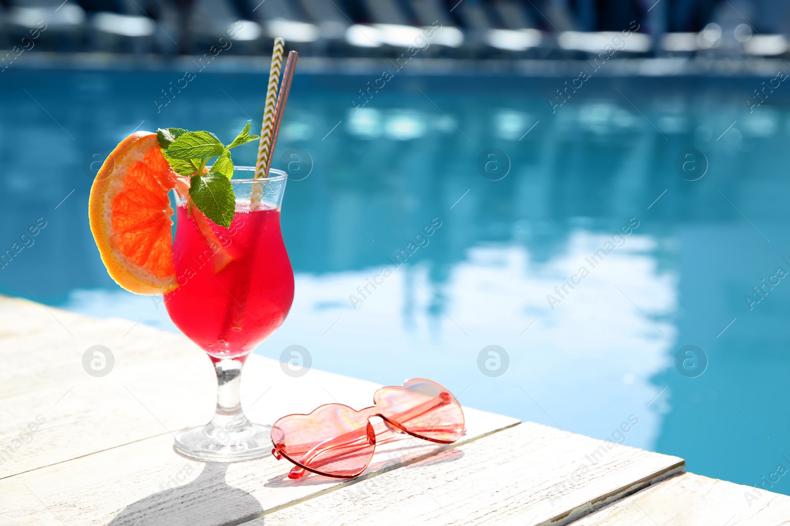 Photo of Refreshing cocktail and sunglasses near outdoor swimming pool on sunny day. Space for text