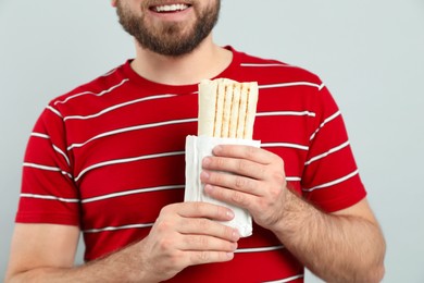 Photo of Young man with delicious shawarma on grey background, closeup