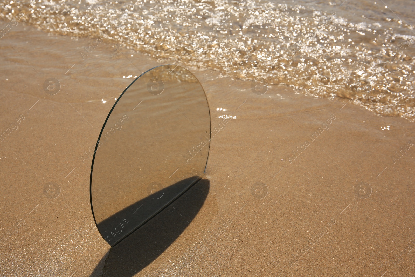 Photo of Round mirror reflecting sea on sandy beach, space for text