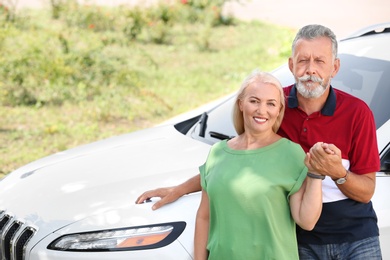 Happy senior couple standing near car outdoors