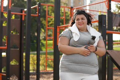 Photo of Beautiful overweight woman with towel and bottle on sports ground