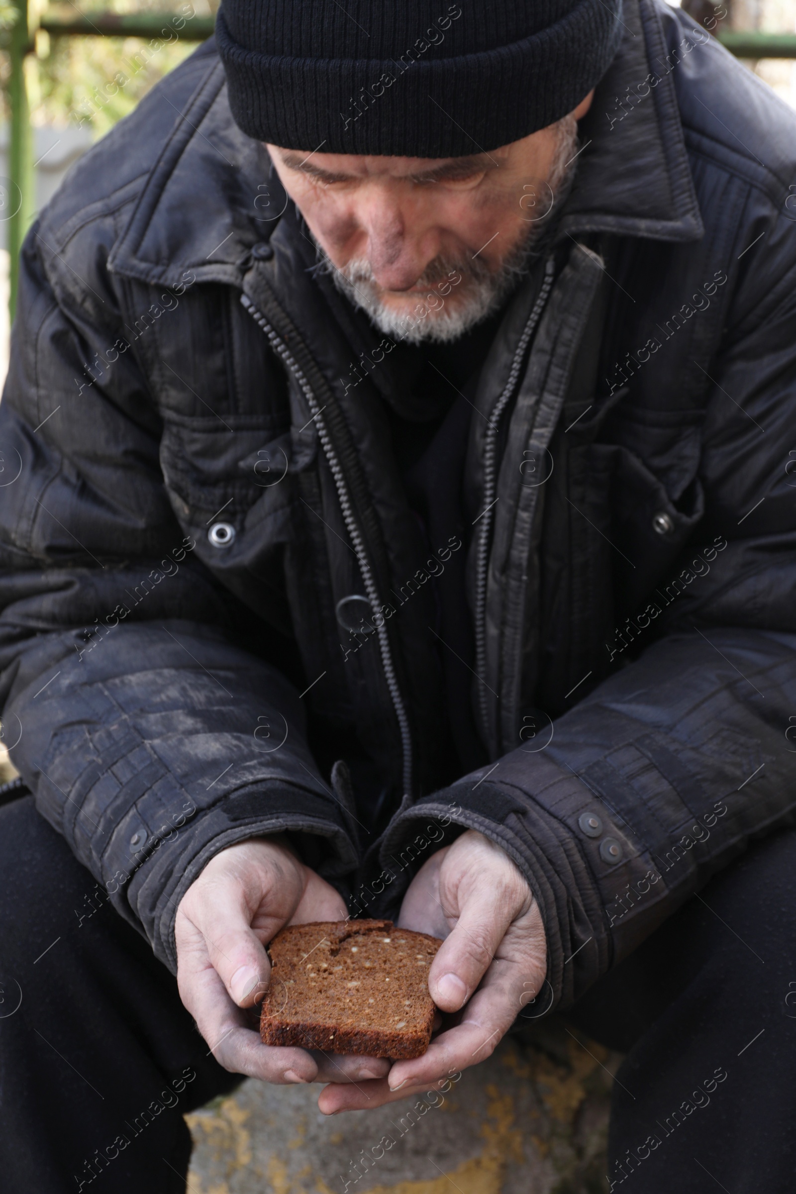 Photo of Poor homeless man holding piece of bread outdoors