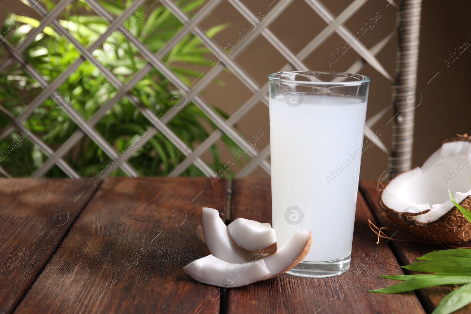 Photo of Glass of coconut water, leaf and nuts on wooden table, space for text