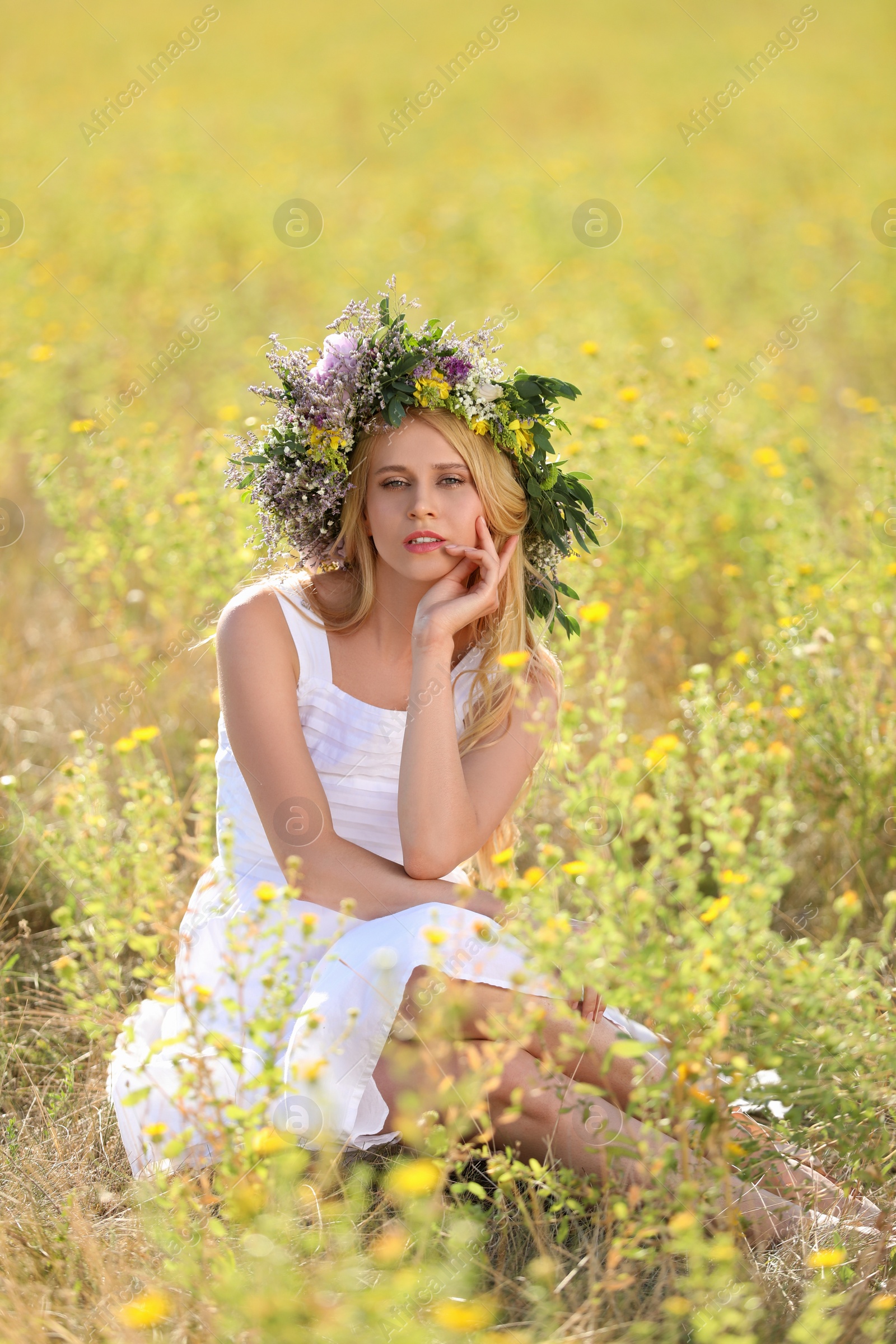 Photo of Young woman wearing wreath made of beautiful flowers in field on sunny day