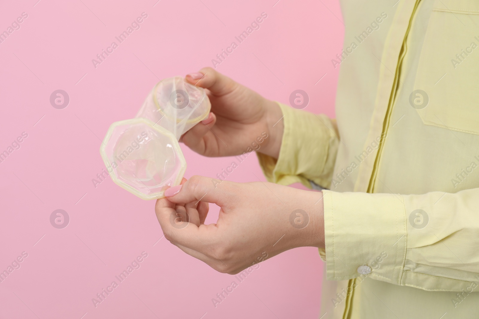 Photo of Woman with unrolled female condom on pink background, closeup. Safe sex