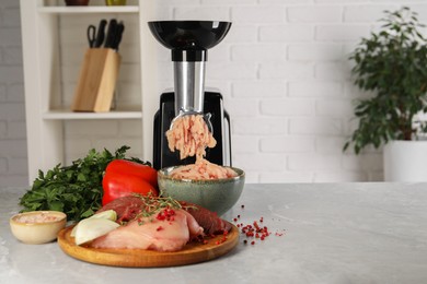 Photo of Electric meat grinder with chicken mince and products on grey marble table indoors. Space for text