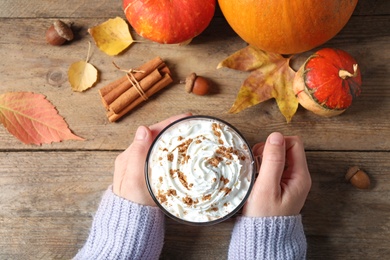 Photo of Woman holding glass cup of tasty pumpkin spice latte at wooden table, top view