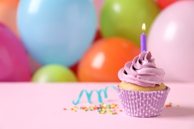 Photo of Birthday cupcake with burning candle and sprinkles on pink table against color balloons. Space for text