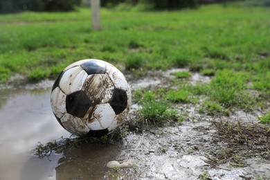 Photo of Dirty soccer ball on green grass near puddle outdoors, space for text