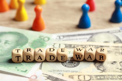 Photo of Wooden cubes with phrase Trade war on different banknotes near colorful pawns, closeup