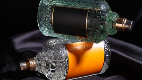 Luxury bottles of perfume on black silk, closeup