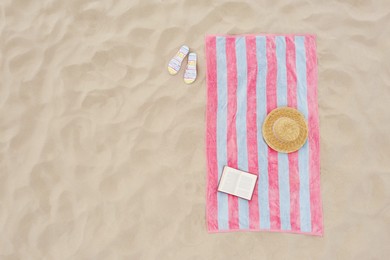 Image of Striped beach towel, book, straw hat and flip flops on sand, aerial view. Space for text