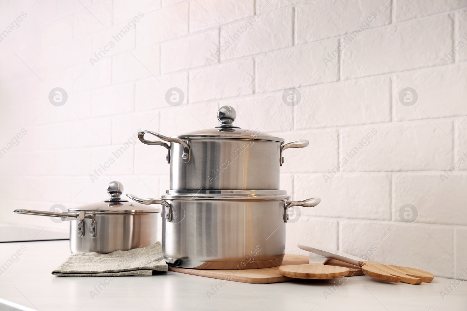 Photo of Set of stainless steel cookware and kitchen utensils on table near white brick wall