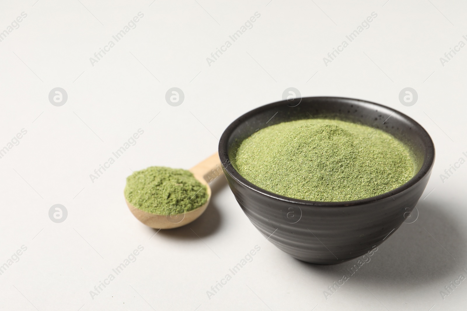 Photo of Wheat grass powder in bowl and spoon on light table