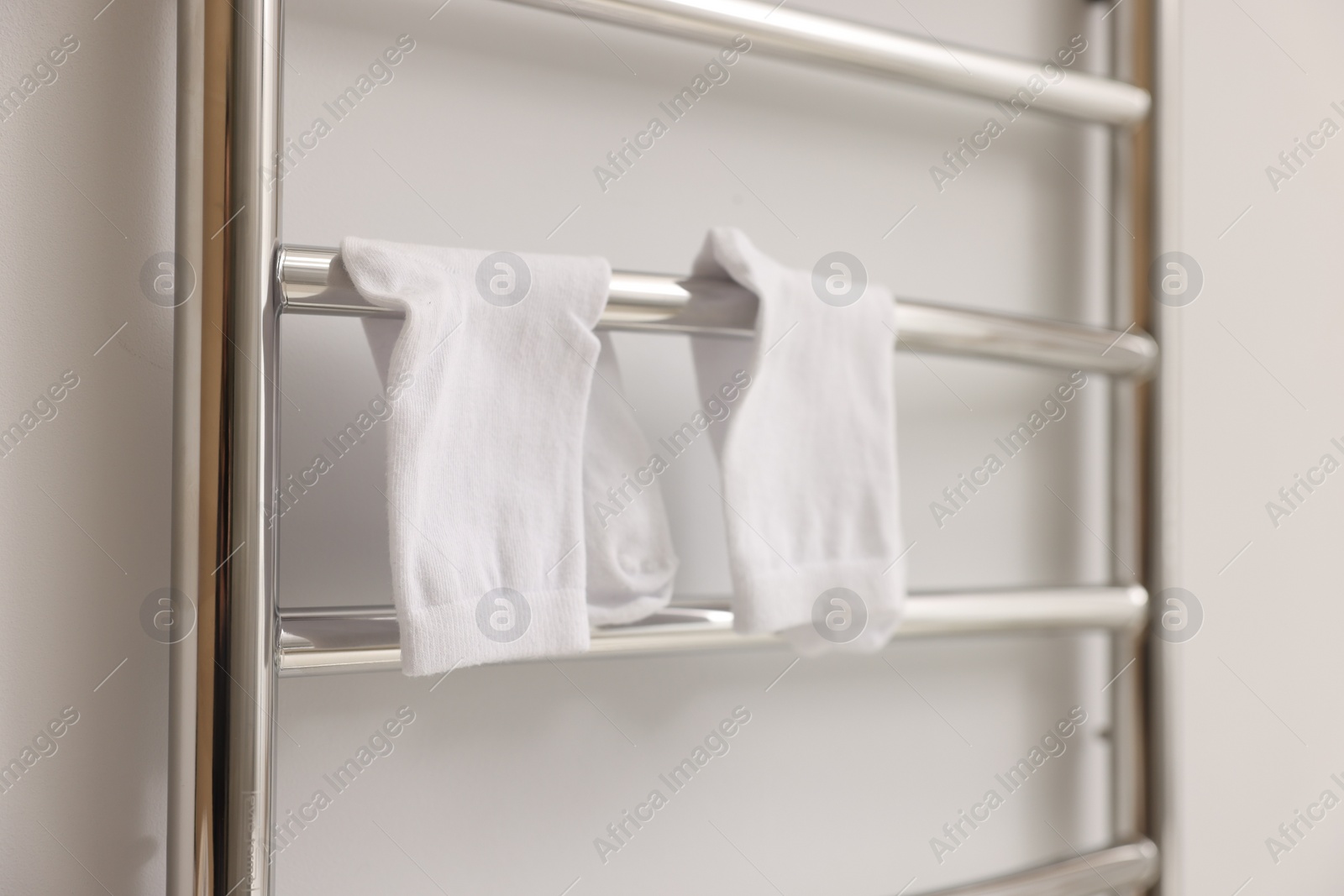 Photo of Heated towel rail with socks on white wall, closeup