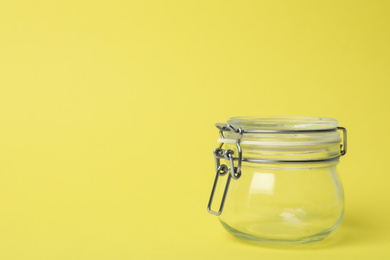 Photo of Closed empty glass jar on light yellow background, space for text