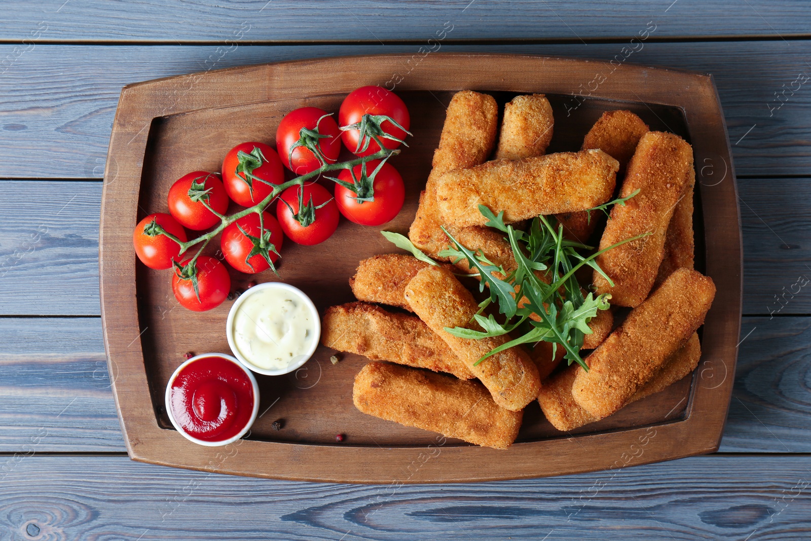 Photo of Board with cheese sticks, sauces and tomatoes on table, top view