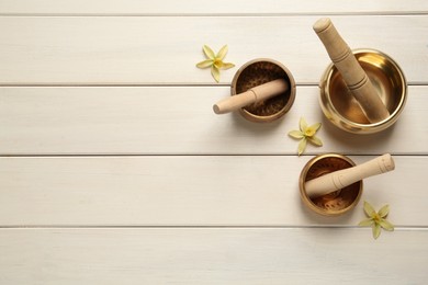 Photo of Golden singing bowls, mallets and flowers on white wooden table, flat lay. Space for text