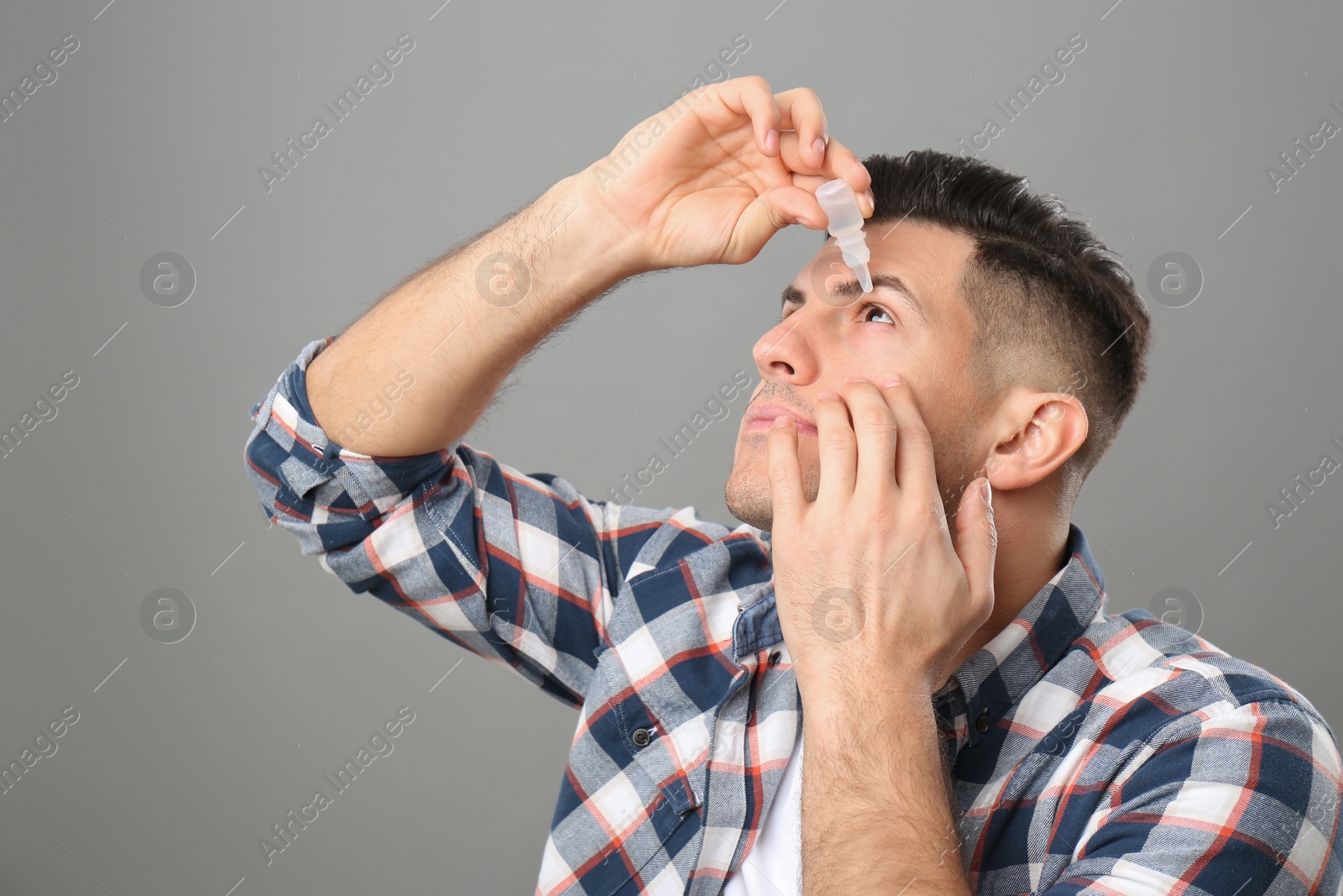 Photo of Man using eye drops on grey background