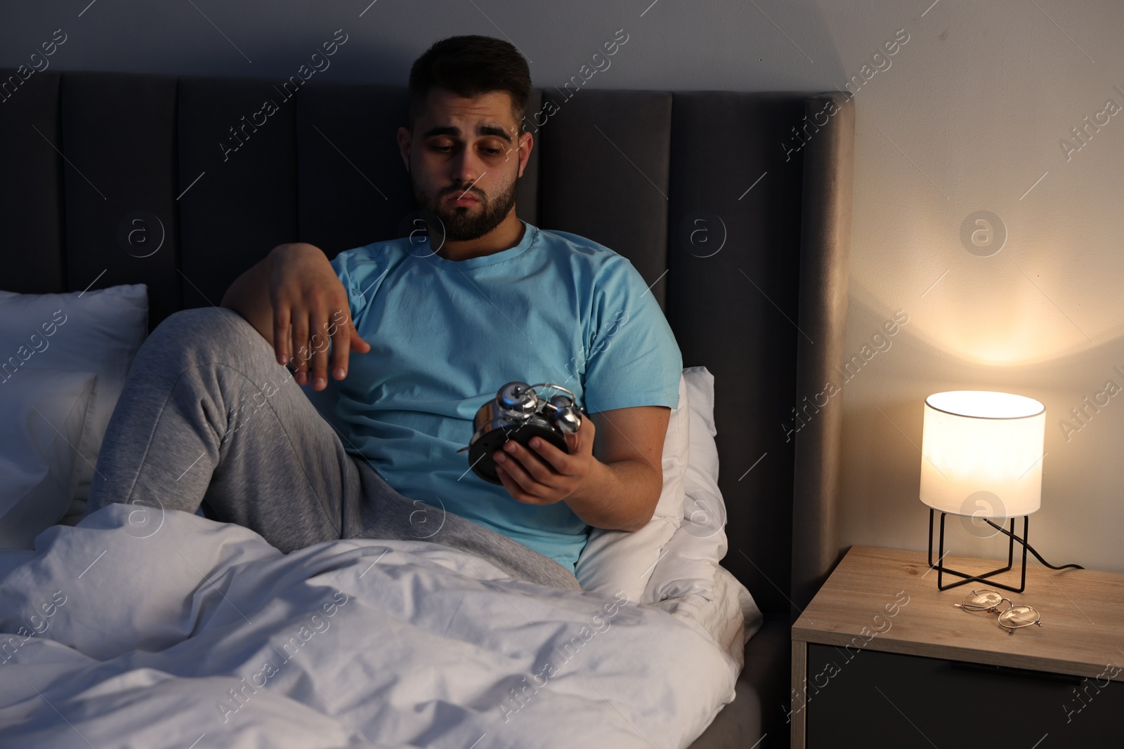 Photo of Tired man looking at alarm clock on bed