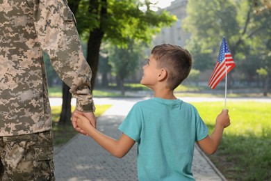 Photo of Soldier and his little son with American flag outdoors, back view. Veterans Day in USA