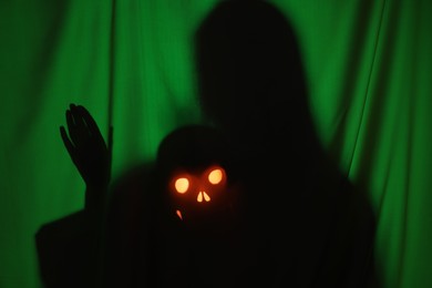 Silhouette of creepy ghost with skull behind dark green cloth