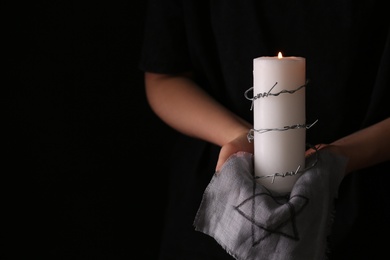 Closeup view of woman holding candle, barbed wire and fabric with David star on black background, space for text. Holocaust memory day