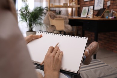 Photo of Woman drawing in sketchbook with pencil at home, closeup