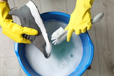 Photo of Woman with gloves and brush cleaning stylish sneakers in wash basin, top view