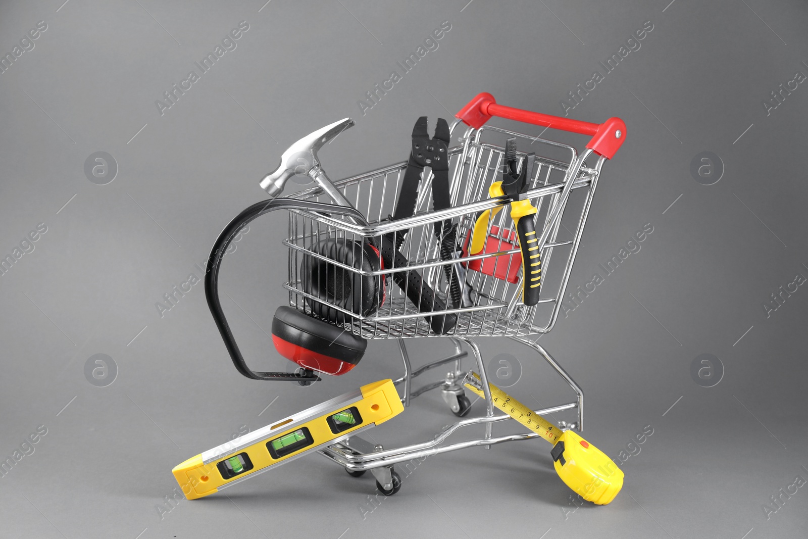 Photo of Small shopping cart with set of construction tools and headphones on grey background