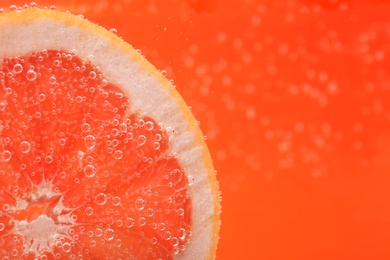 Photo of Slice of grapefruit in sparkling water on orange background, closeup with space for text. Citrus soda