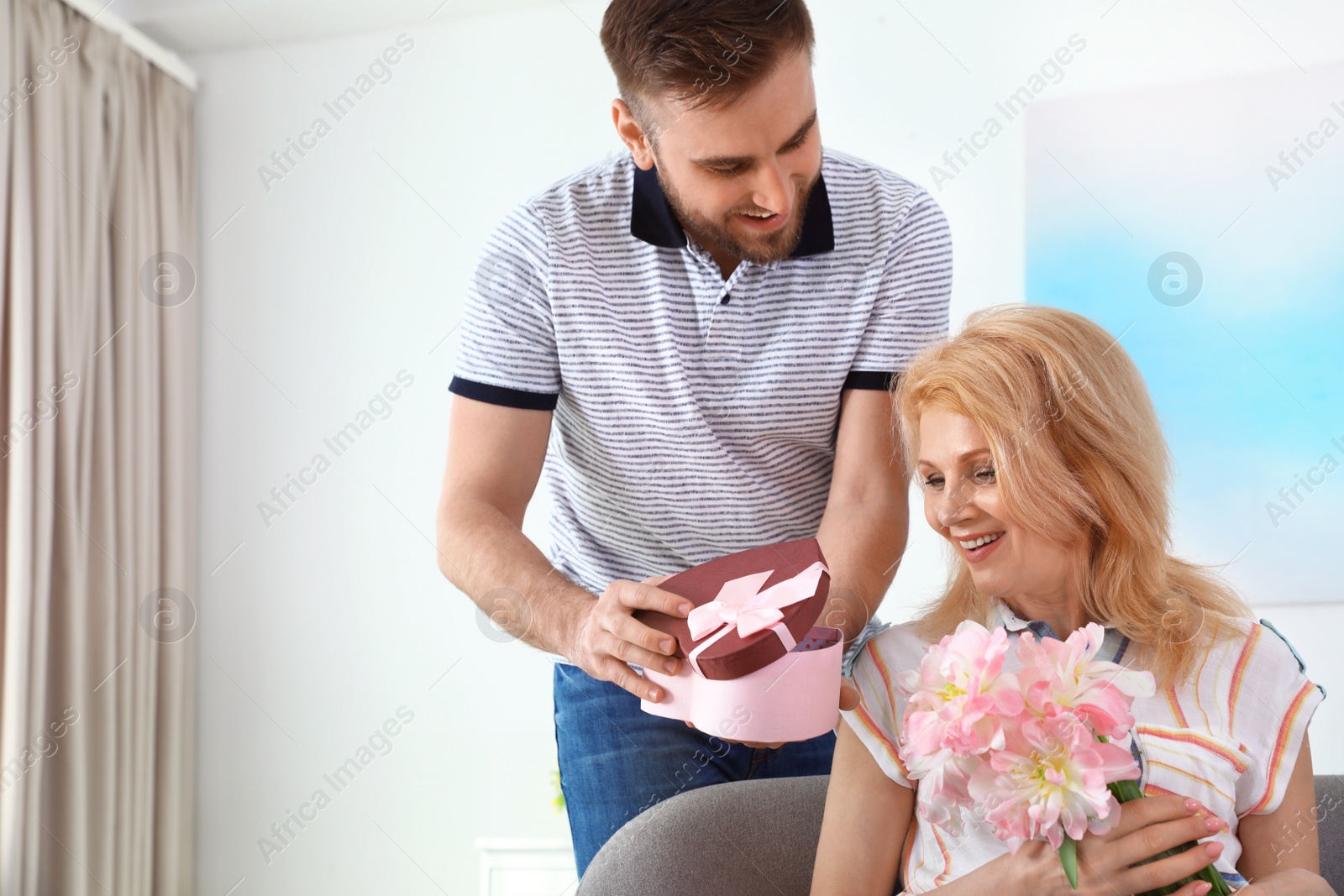 Photo of Young man congratulating his mature mom at home, space for text. Happy Mother's Day