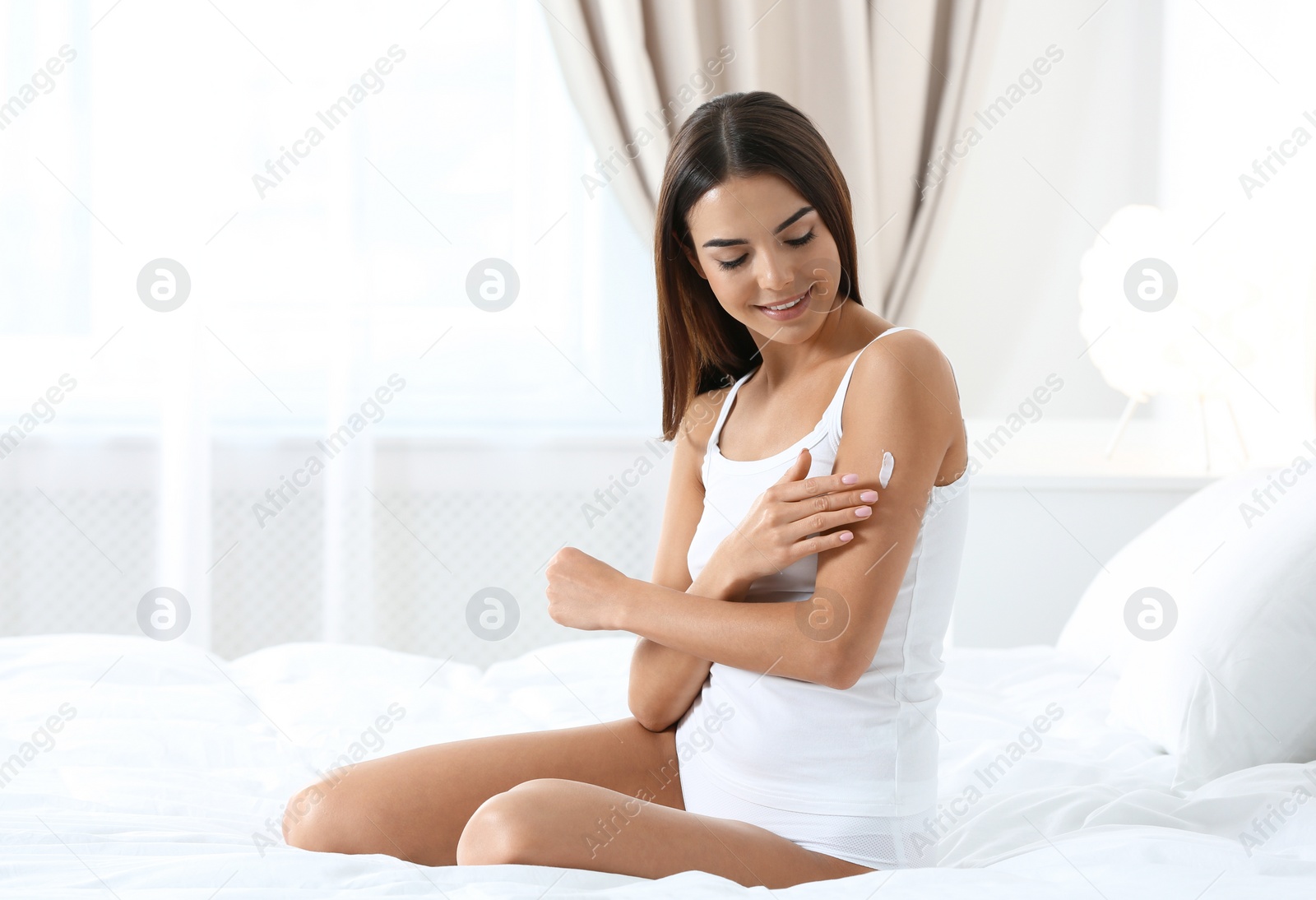 Photo of Young woman with perfect smooth skin applying cream indoors. Beauty and body care