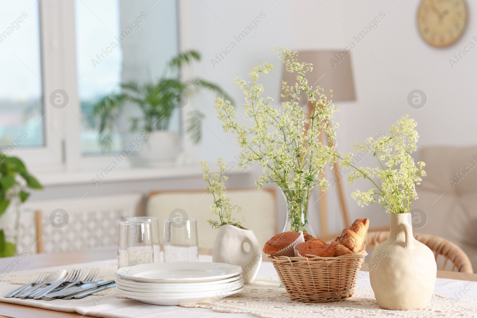 Photo of Clean dishes, flowers and fresh pastries on table in stylish dining room