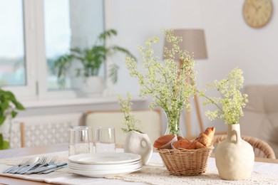 Photo of Clean dishes, flowers and fresh pastries on table in stylish dining room