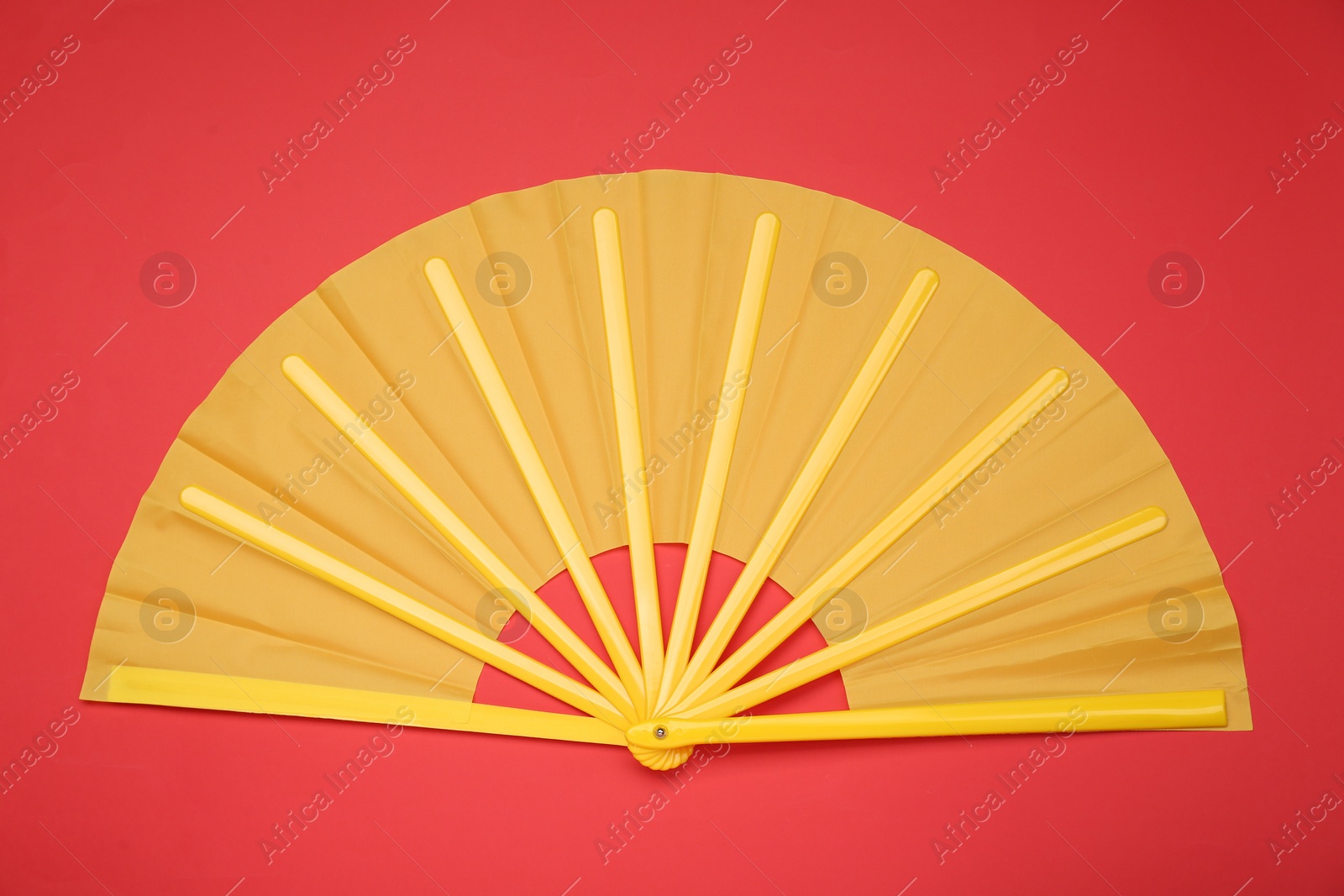 Photo of Bright yellow hand fan on red background, top view