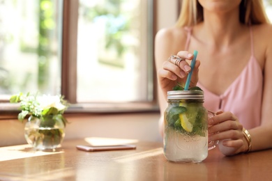 Photo of Young woman with mason jar of tasty natural lemonade in cafe. Detox drink