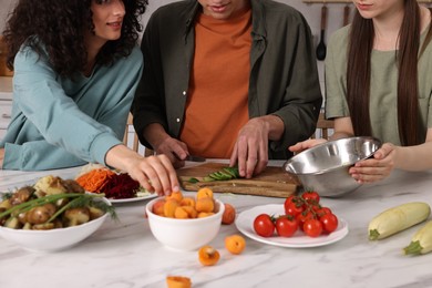 Friends cooking healthy vegetarian meal at white marble table in kitchen, closeup