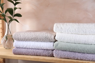 Photo of Stacked soft towels and green leaves on wooden shelf indoors