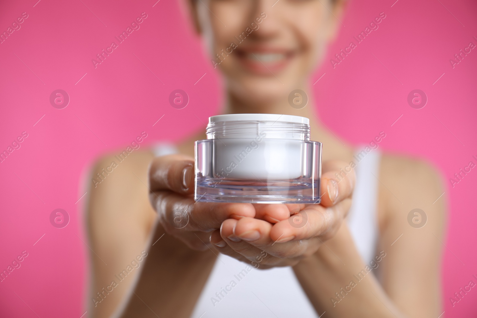 Photo of Woman holding jar of facial cream on pink background, closeup