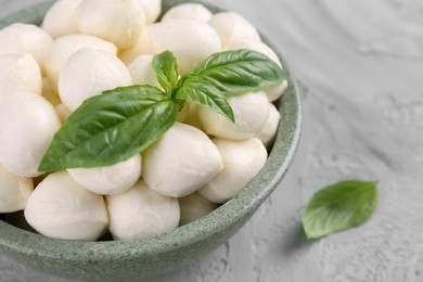 Photo of Tasty mozzarella balls and basil leaves in bowl on grey table, closeup. Space for text
