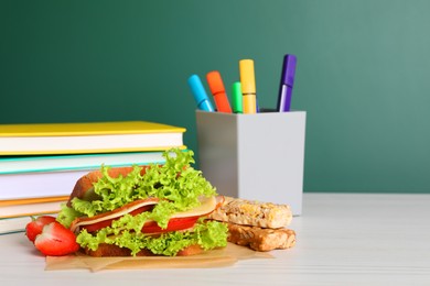 Tasty healthy food and different stationery on white wooden table near green chalkboard, space for text. School lunch
