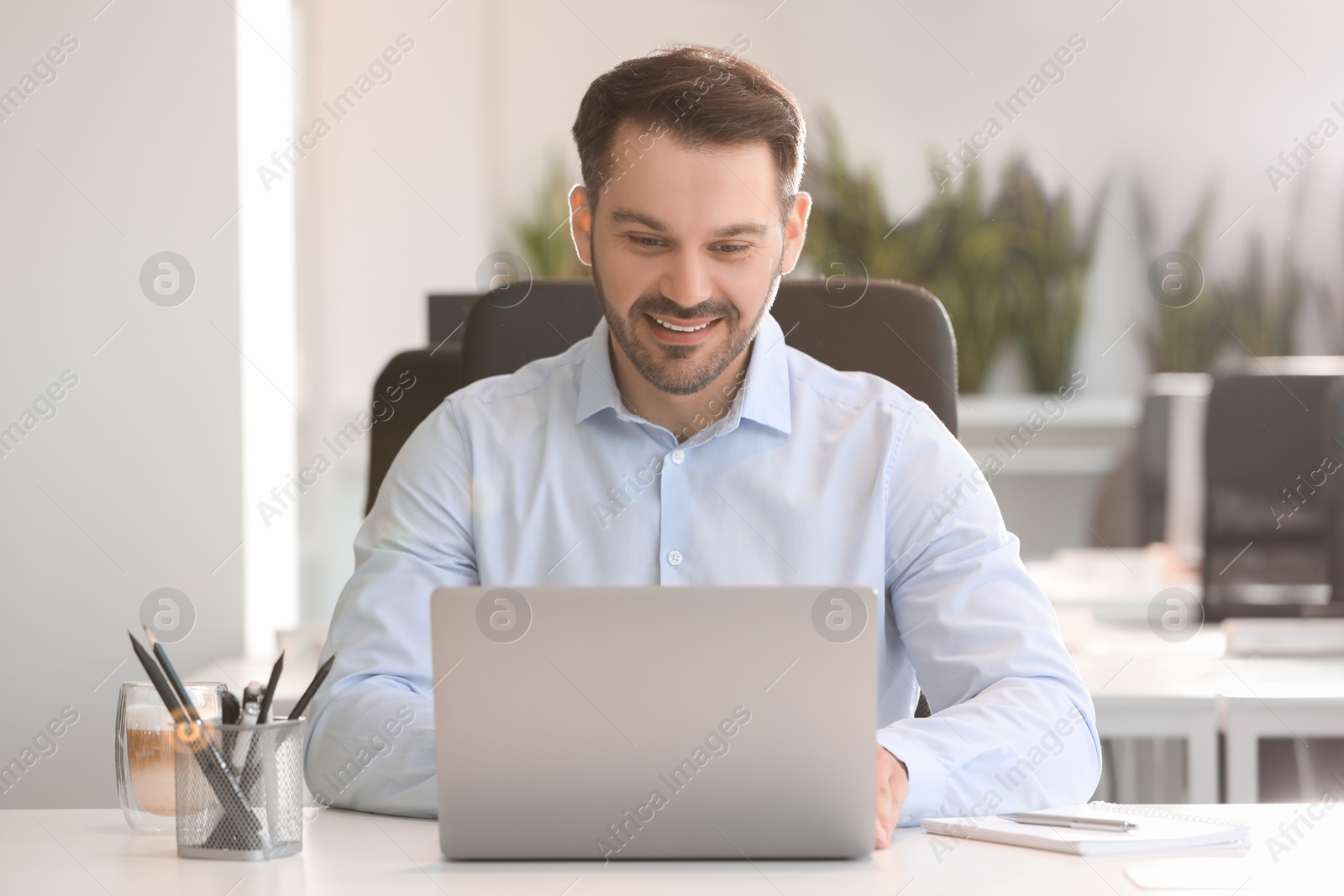 Photo of Happy man using modern laptop at white desk in office