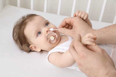 Father cleaning nose of his baby with cotton bud on bed, closeup