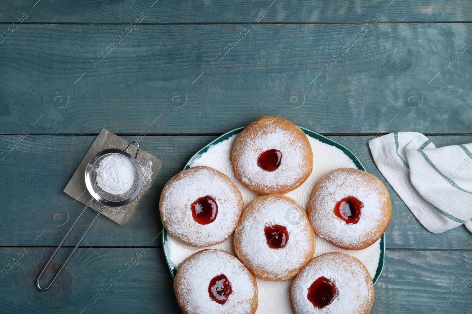 Photo of Hanukkah doughnuts with jelly and sugar powder served on blue wooden table, flat lay